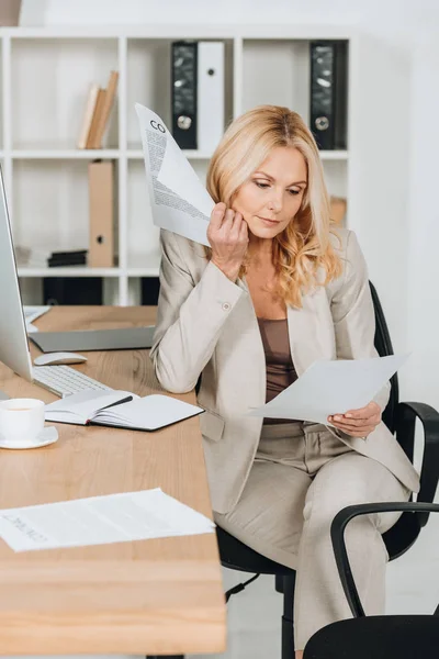 Mujer de negocios madura grave que trabaja con papeles mientras está sentado en el lugar de trabajo - foto de stock