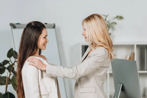 Вид збоку зрілої бізнес-леді, що підтримує усміхнену молоду жінку-колегу в офісі — стокове фото