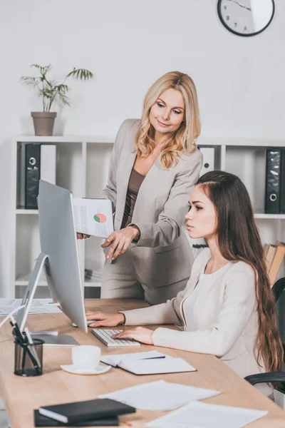 Jeune femme d'affaires utilisant un ordinateur de bureau et un mentor féminin mature pointant vers l'écran — Photo de stock