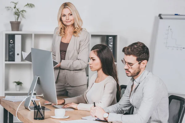 Reife Geschäftsfrau hält Ordner in der Hand und blickt auf junge Geschäftsleute, die im Büro arbeiten — Stockfoto