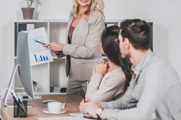 Tiro cortado de empresária mostrando gráficos e gráficos para jovens colegas no escritório — Fotografia de Stock