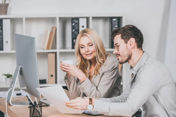 Smiling professional businesspeople working with papers while sitting together at desk — Stock Photo