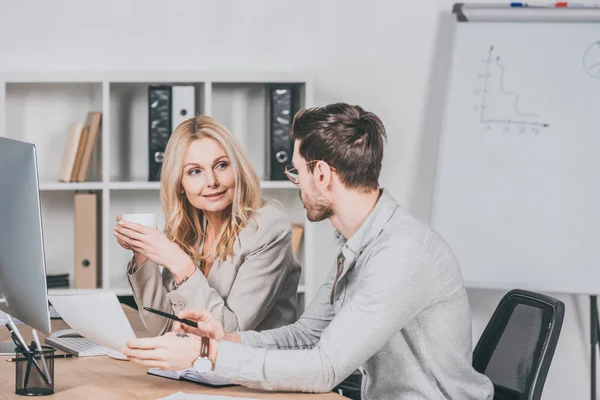 Professional businesspeople working with papers and looking at each other while sitting together at desk — Stock Photo