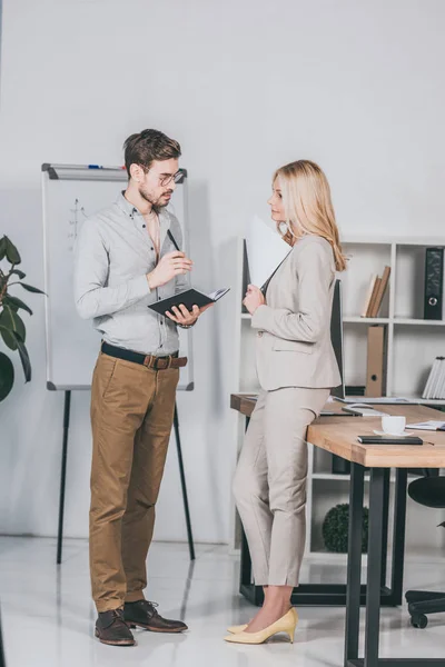 Focused young businessman holding notebook and looking at mature female mentor in office — Stock Photo