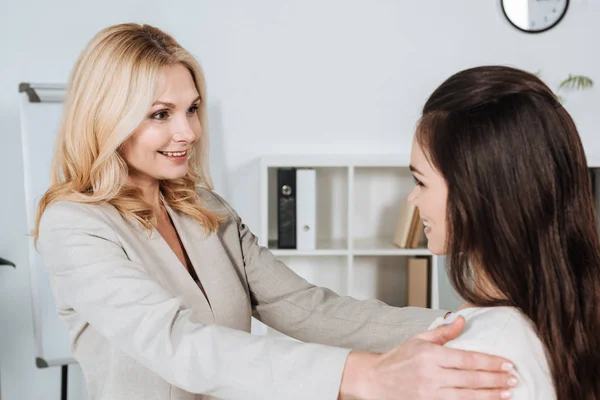 Seitenansicht schön lächelnder Geschäftsfrauen, die im Büro stehen und einander anschauen — Stockfoto