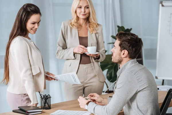 Donna d'affari matura in possesso di una tazza di caffè e guardando i giovani colleghi che lavorano con contratto in carica — Foto stock