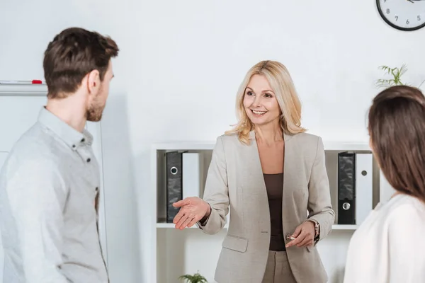 Smiling professional business mentor looking at young colleagues in office — Stock Photo