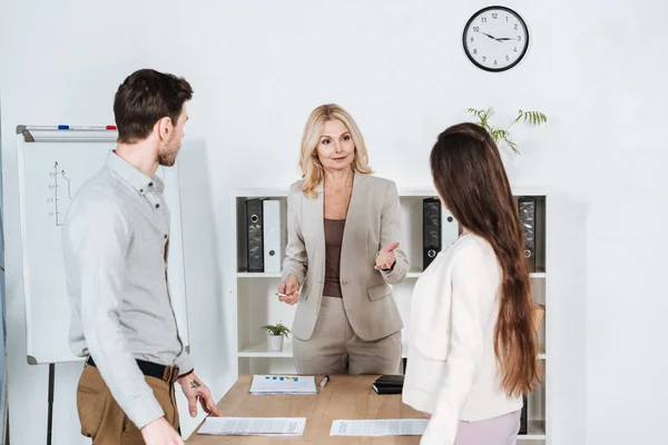 Professional mature businesswoman standing and talking with young colleagues in office — Stock Photo