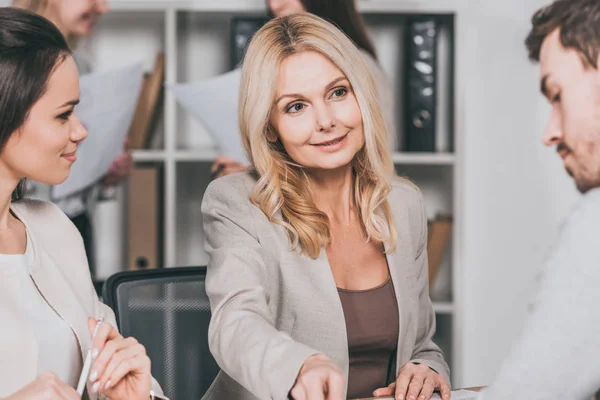 Beautiful smiling mature businesswoman working with young colleagues in office — Stock Photo