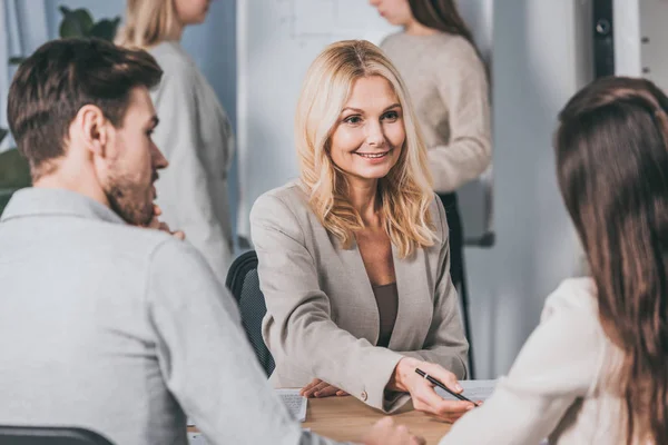 Lächelnde reife Geschäftsfrau, die junge Kollegen bei der gemeinsamen Arbeit im Büro betrachtet — Stockfoto