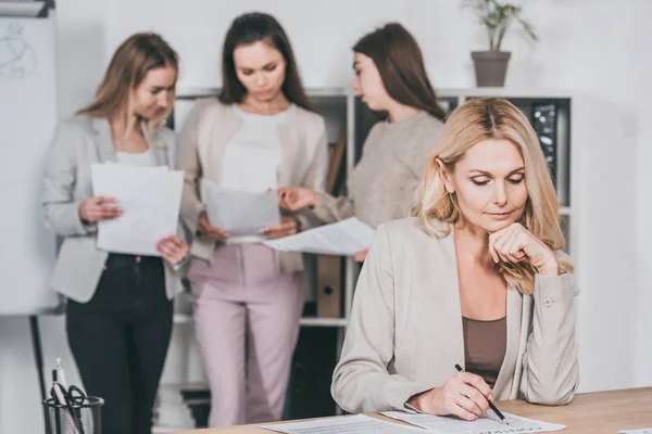 Mature femme d'affaires travaillant avec contrat et les jeunes femmes d'affaires discuter des documents derrière dans le bureau — Photo de stock