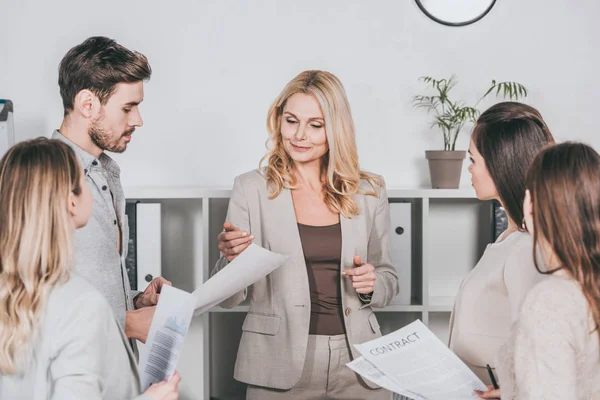 Professional business mentor looking at papers and working with young colleagues in office — Stock Photo