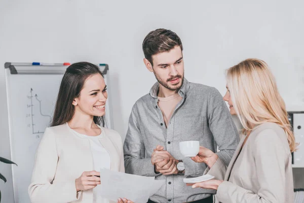 Mentor d'affaires souriant tenant une tasse de café et parlant avec de jeunes collègues au bureau — Photo de stock