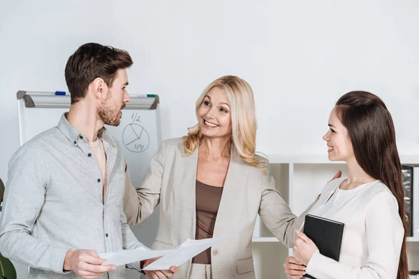 Smiling mature businesswoman looking at young colleagues with notebook and papers in office — Stock Photo