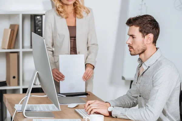 Cropped shot of business mentor holding papers and young businessman using desktop computer in office — Stock Photo