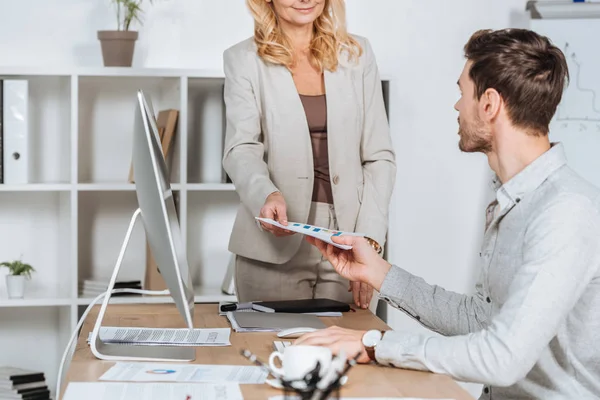 Cropped shot of coworkers holding paper with business charts above desk in office — Stock Photo