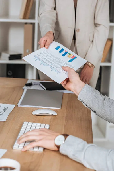 Tiro recortado de empresários segurando papel com gráficos e gráficos acima mesa no escritório — Fotografia de Stock