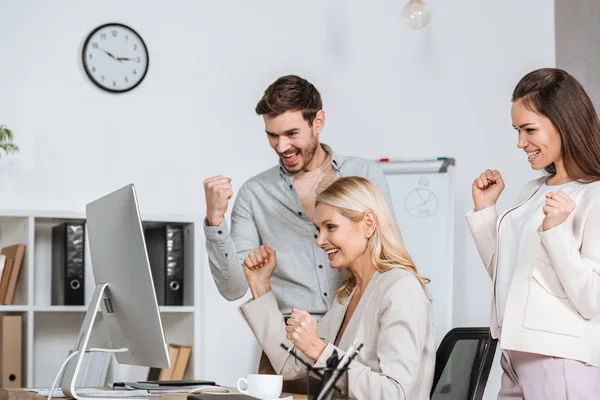 Mentor de negócios animado com colegas balançando punhos e olhando para o computador desktop no escritório — Fotografia de Stock