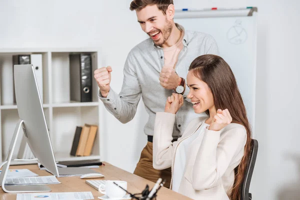 Fröhliche junge Geschäftskollegen, die im Büro die Fäuste schütteln und auf den Desktop-Computer schauen — Stockfoto