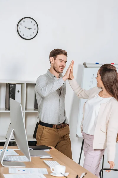 Glückliche junge Geschäftskollegen geben High Five und lächeln sich am Arbeitsplatz an — Stockfoto