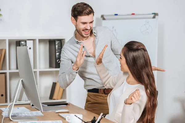 Jóvenes empresarios felices dando cinco y sonriéndose en el lugar de trabajo - foto de stock