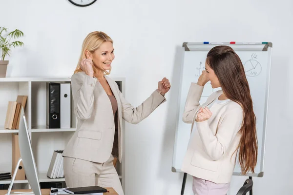 Fröhliche Geschäftsfrauen triumphieren und lächeln einander im Amt zu — Stockfoto