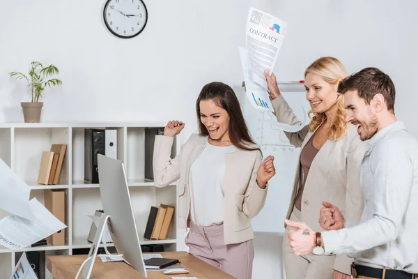 Empresarios emocionados agitando los puños y mirando a la computadora de escritorio en la oficina - foto de stock