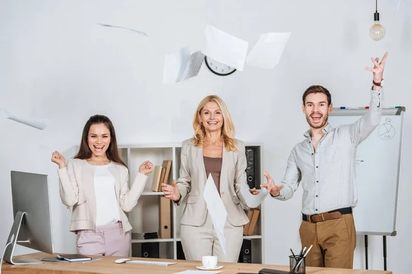 Веселі професійні бізнесмени кидають папери і посміхаються на камеру в офісі — стокове фото