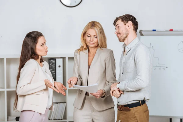 Female mentor holding papers and working with frustrated young colleagues in office — Stock Photo