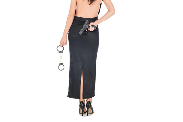 Back view of female secret agent in black dress holding gun and handcuffs, isolated on white — Stock Photo