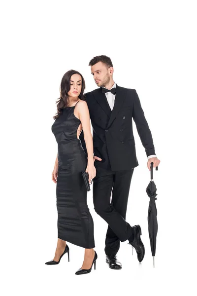 Beau couple de tueurs en vêtements noirs posant avec pistolet et parapluie, isolé sur blanc — Photo de stock