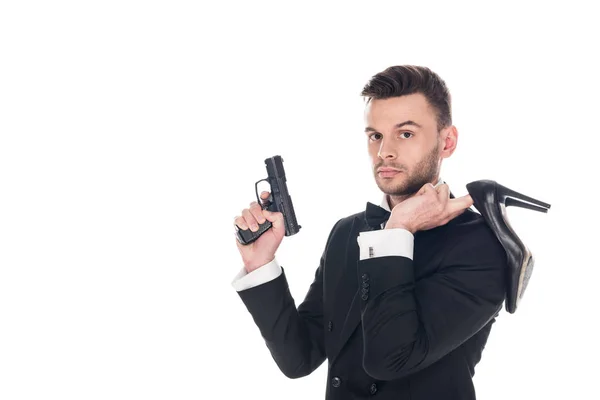 Guapo agente secreto en traje negro sosteniendo pistola y tacones altos, aislado en blanco - foto de stock