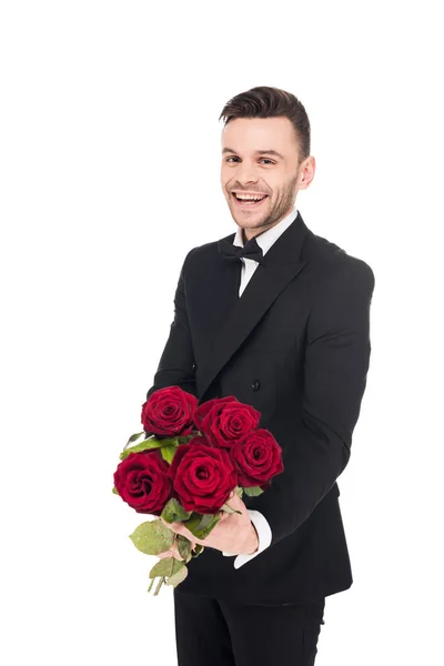 Guapo hombre alegre en chaqueta negra regalando flores de rosa roja para el día de San Valentín, aislado en blanco - foto de stock
