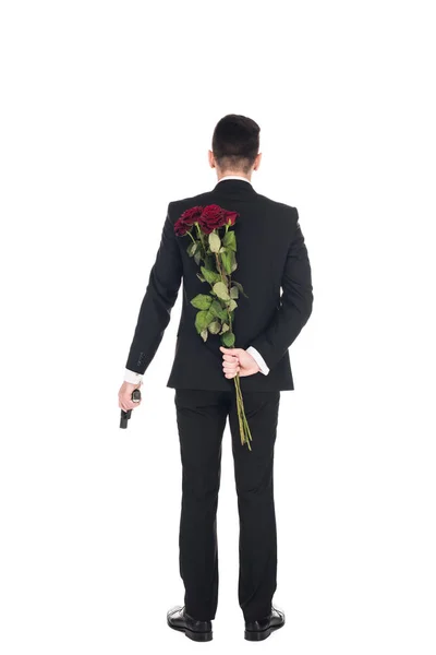 Vista trasera del agente secreto en traje negro sosteniendo pistola y rosas rojas, aislado en blanco - foto de stock