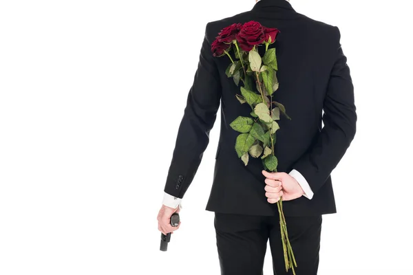 Vista trasera de asesino en traje negro sosteniendo pistola y flores de color rosa rojo, aislado en blanco — Stock Photo