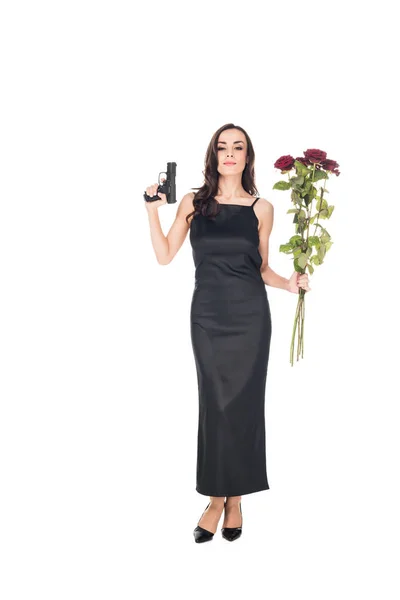 Happy elegant secret agent in black dress holding gun and red roses, isolated on white — Stock Photo