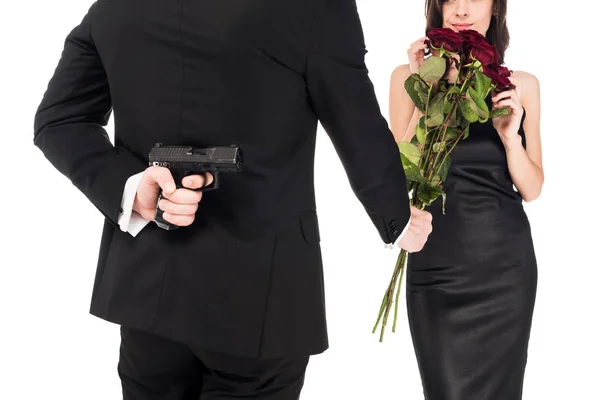 Vista posteriore dell'uomo che dona rose rosse mentre nasconde pistola dietro la schiena, isolato su bianco — Foto stock