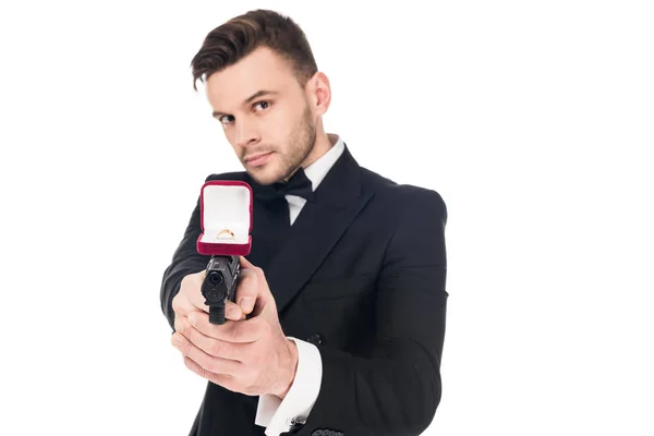 Handsome secret agent in black suit aiming with handgun with proposal ring, isolated on white — Stock Photo