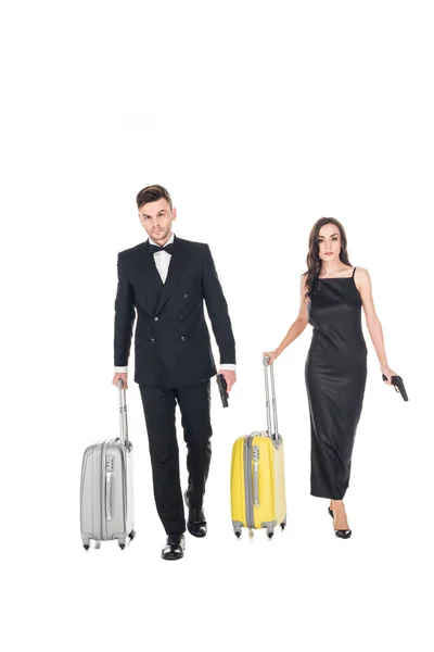 Elegante pareja de agentes secretos vestidos de negro con pistolas y bolsas de viaje, aislados en blanco - foto de stock