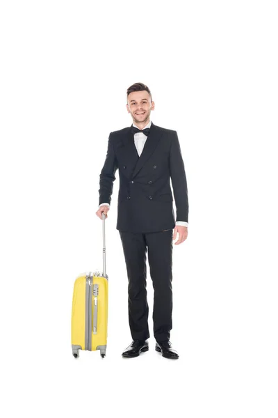Sonriente hombre elegante en esmoquin negro posando con bolsa de viaje aislada en blanco - foto de stock