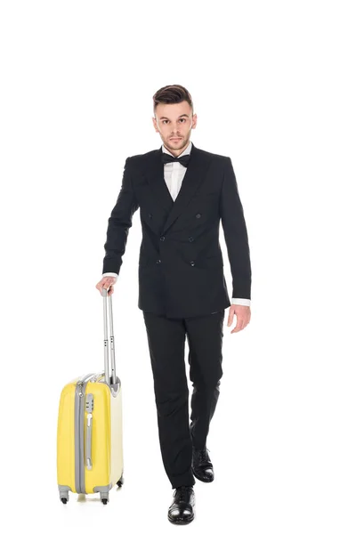 Guapo turista en esmoquin negro caminando con maleta aislada en blanco - foto de stock