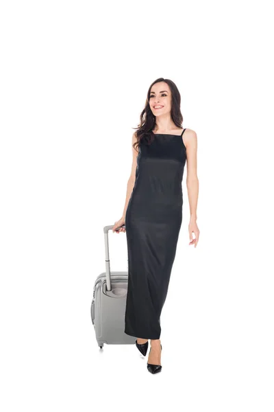 Glücklich elegante Reisende in schwarzem Kleid mit Koffer isoliert auf weiß zu Fuß — Stockfoto