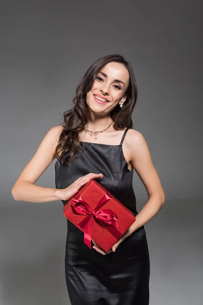 Belle femme souriante tenant boîte cadeau rouge isolé sur gris — Photo de stock