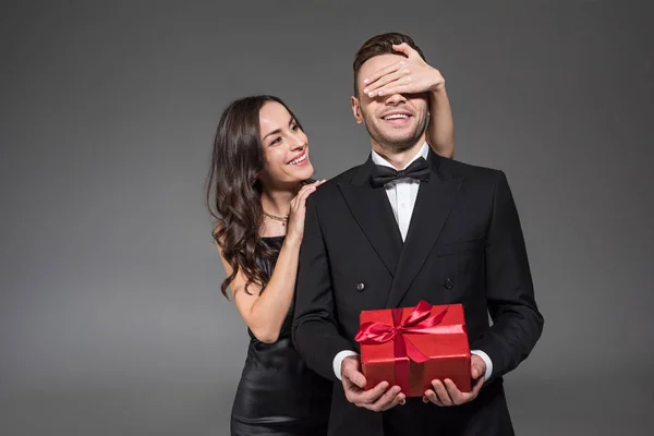 Beautiful woman closing eyes and making surprise to boyfriend with present on valentines day, isolated on grey — Stock Photo