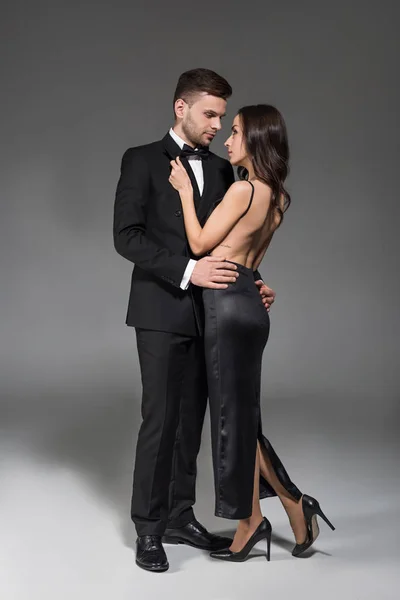 Beau couple en noir vêtements câlins sur gris — Photo de stock