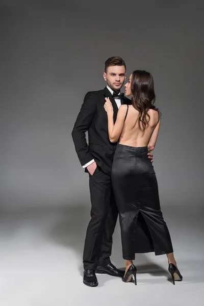 Красива елегантна пара в чорному одязі обіймається на сірому — стокове фото