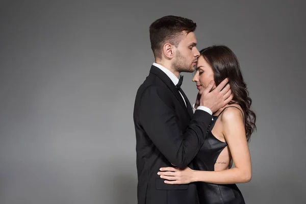 Handsome man kissing forehead of beautiful girlfriend isolated on grey — Stock Photo