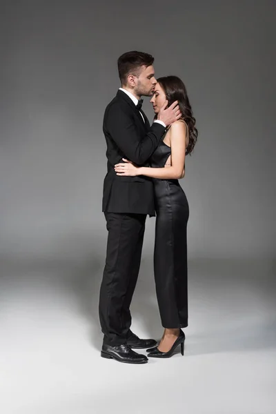 Giovane tenero uomo baciare fronte di bella fidanzata su grigio — Foto stock