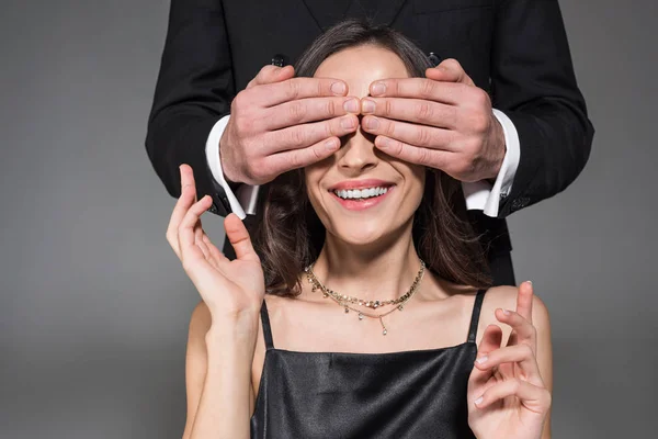 Mann macht Überraschung und schließt Augen einer glücklichen Freundin am Valentinstag, isoliert auf grau — Stockfoto