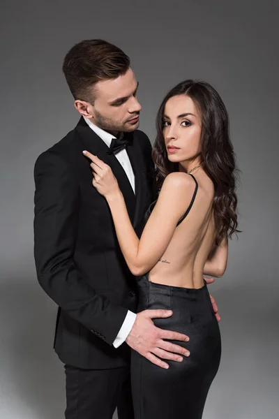 Elegante pareja en negro ropa abrazos juntos aislado en gris - foto de stock